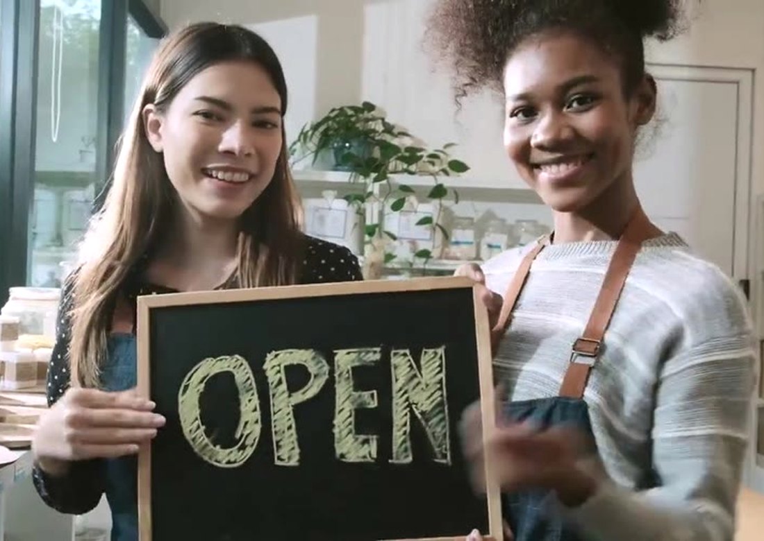 Two small business owners holding an OPEN sign at their new location