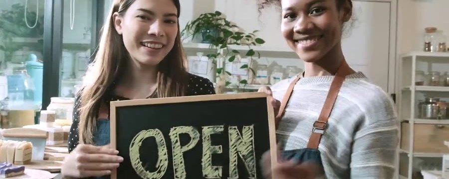 Two small business owners holding an OPEN sign at their new location
